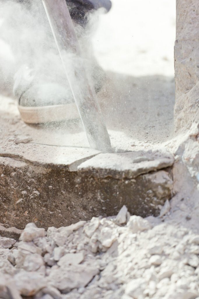 Demolition worker breaking concrete with a jackhammer at a construction site.