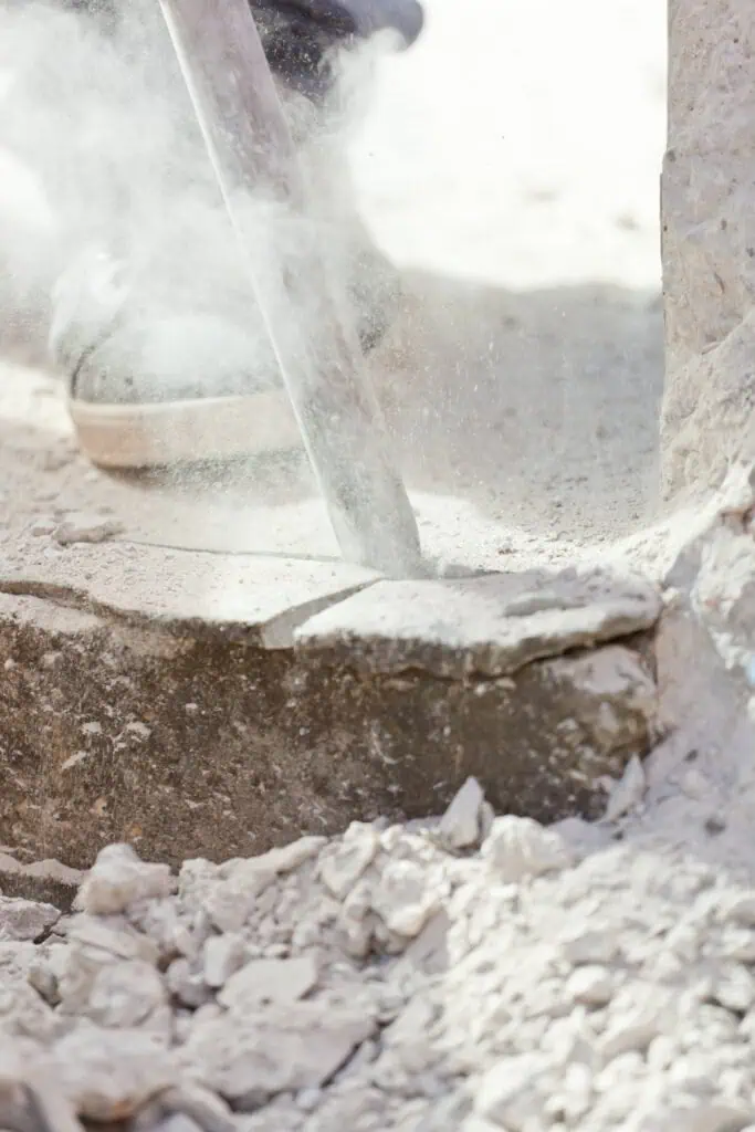 Demolition worker breaking concrete with a jackhammer at a construction site.