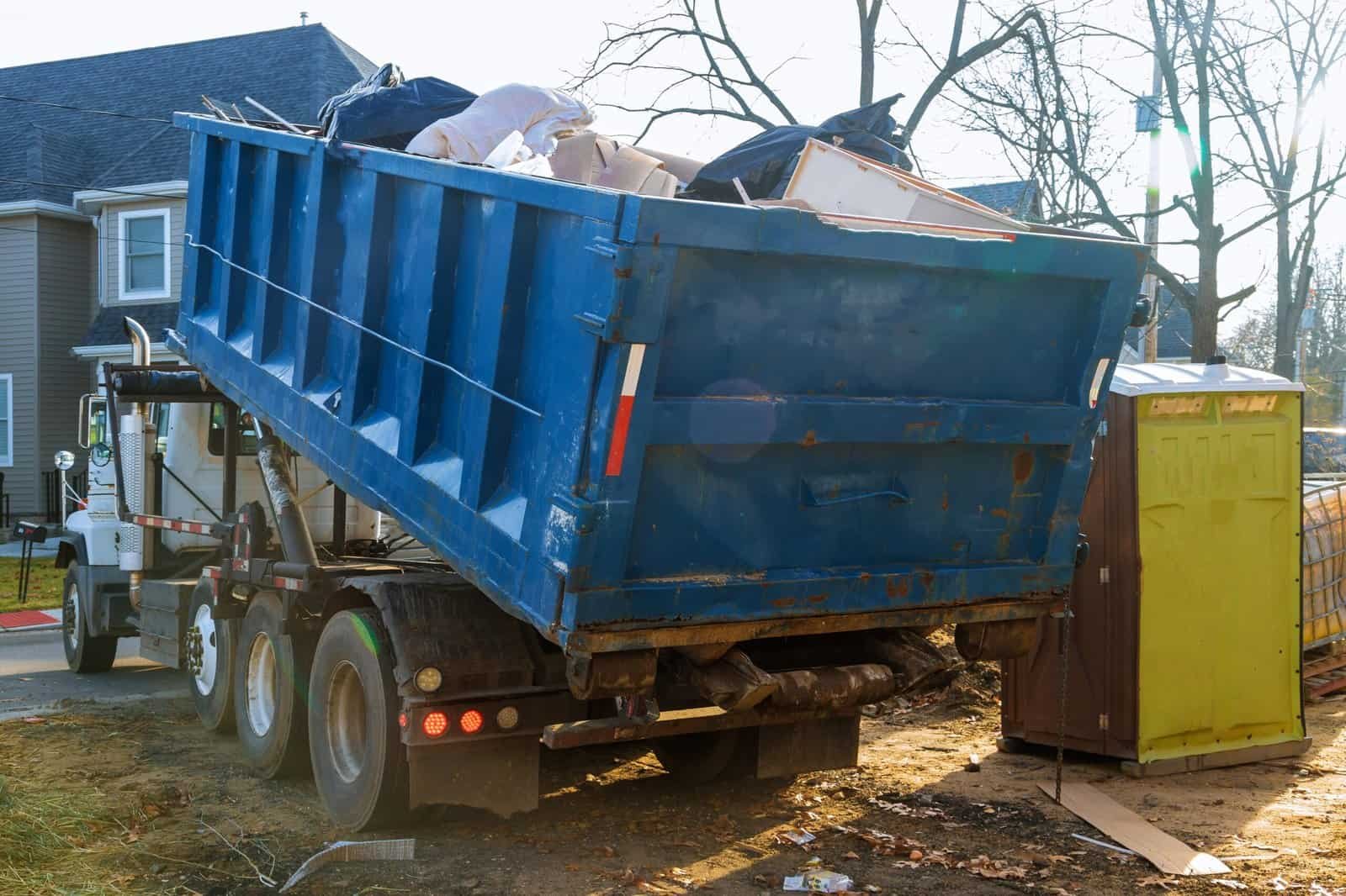 Demolition debris being loaded into a large blue dumpster truck.